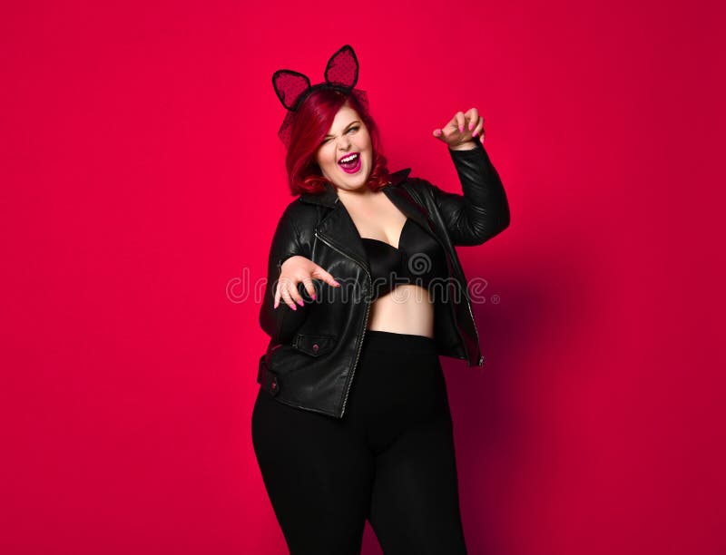 Cute sexy plus size brunette with black bunny ears in leather jacket and underwear posing on red background