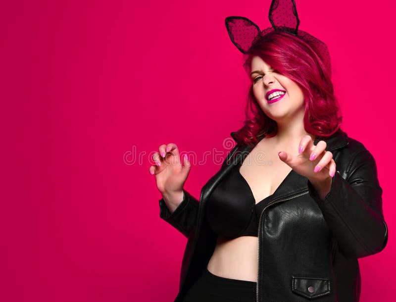 Cute sexy plus size brunette with black bunny ears in leather jacket and underwear posing on red background