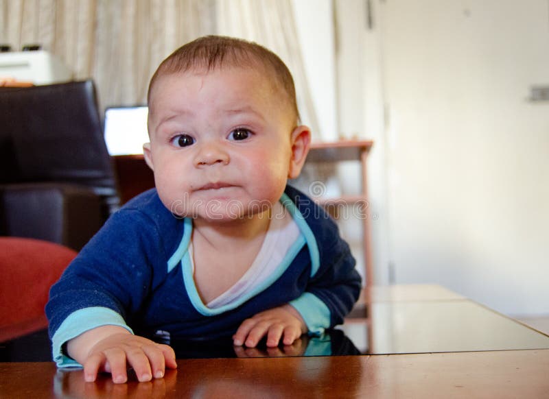 Cute six months old baby boy drooling on the flor and making funny faces - early development concept