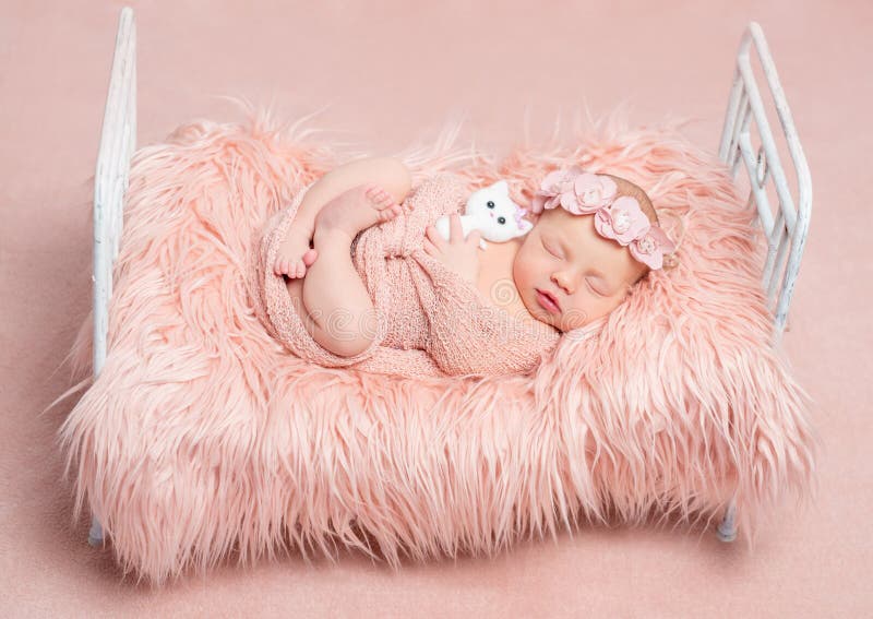 Cute sleeping newborn girl with toy cat on little bed