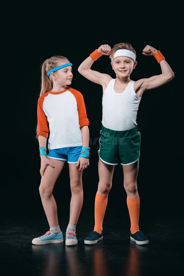 Cute smiling boy and girl in sportswear standing together isolated on black