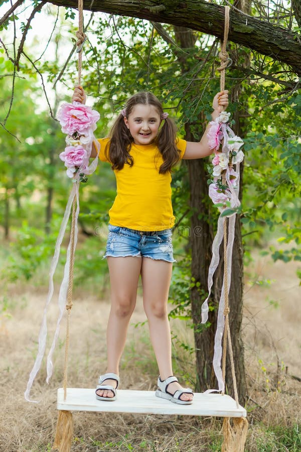 Cute smiling girl having fun on a swing in tree forest