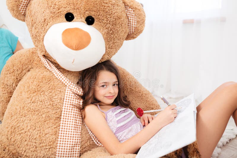 Cute smiling girl lying on big plush bear and drawing royalty free stock photo Cute smiling girl lying on big plush bear and drawing royalty free stock photo
