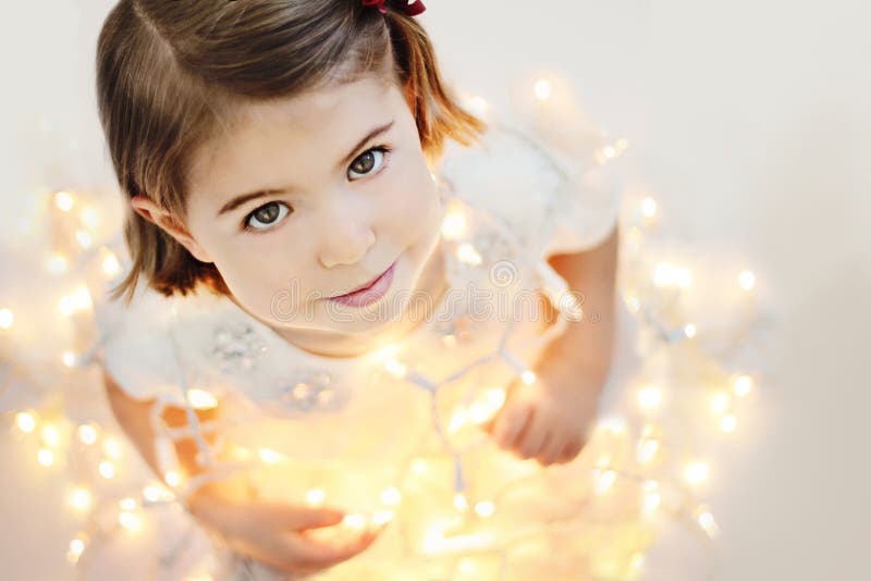 Roztomilé, usměvavé, šťastné tři roky stará dívka sedí s zářící Vánoční osvětlení.