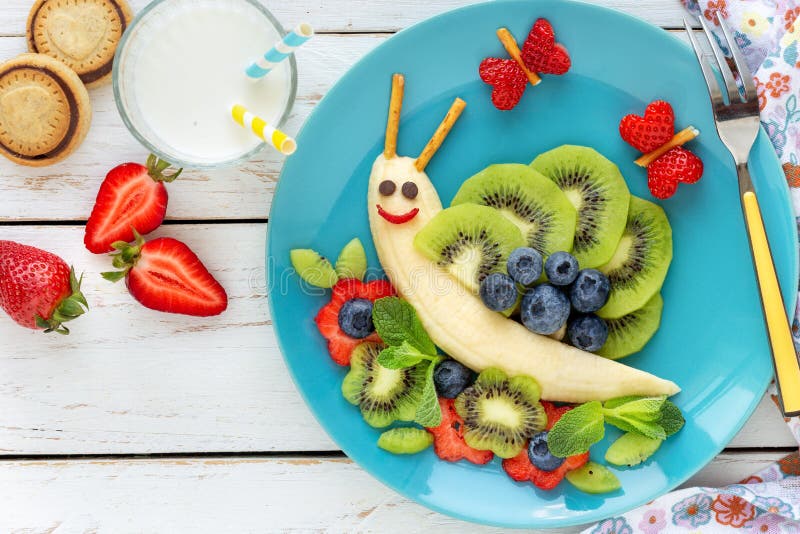 Cute smilingfresh  fruit snail for kids breakfast. Fun food for kids - cute smiling snail made of fresh fruits bananas, kiwi, blueberries and strawberries as a