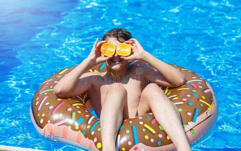 Cute sporty boy swims in the pool with donut ring and has fun, smiles, holds oranges. vacation with kids, holidays stock photos Cute sporty boy swims in the pool with donut ring and has fun, smiles, holds oranges. vacation with kids, holidays stock photos