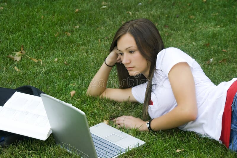 Cute teen girl laying down on the grass studying royalty free stock photography