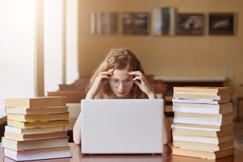 Cute teenage girl with glasses, surrounded by books and school work, looking frustrated and tired, spending time in library, 库存图片 Cute teenage girl with glasses, surrounded by books and school work, looking frustrated and tired, spending time in library, 库存图片