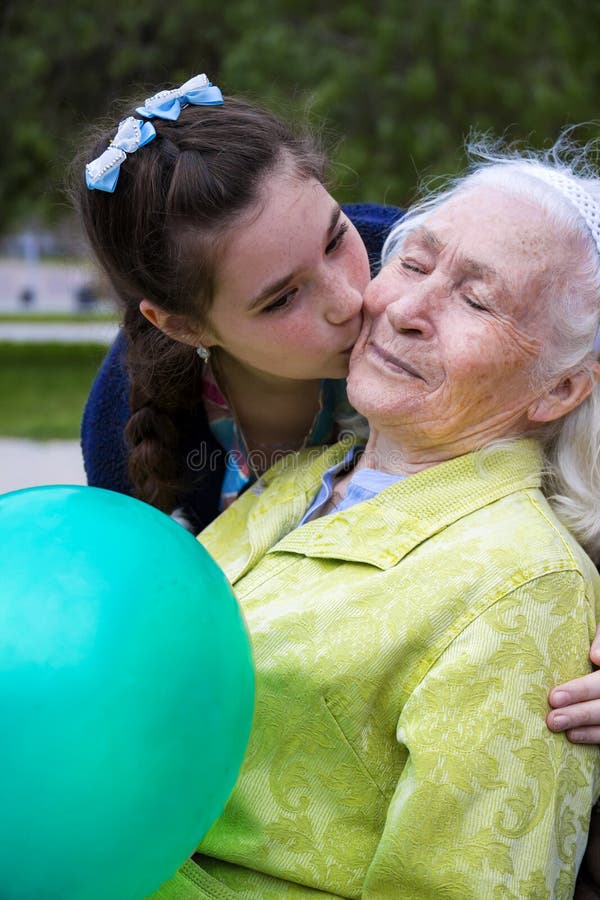 Cute teenage girl is kissing her beautiful smiling granny in cheek. 