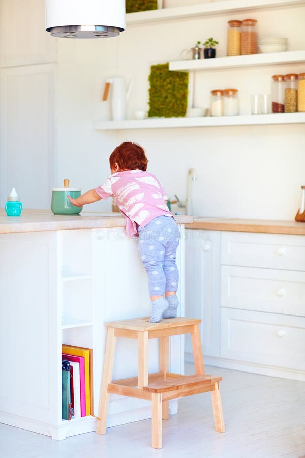 Cute toddler baby climbs on step stool, trying to reach things on the high desk in the kitchen royalty free stock photography Cute toddler baby climbs on step stool, trying to reach things on the high desk in the kitchen royalty free stock photography