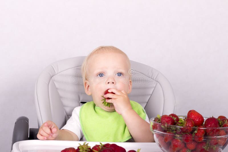 Cute toddler eating strawberry. Funny baby boy with a strawberry in his arm