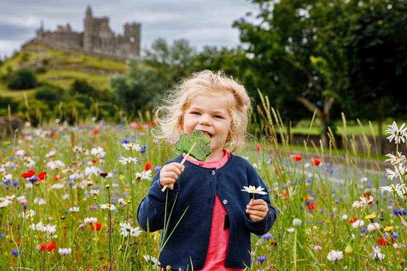 Cute toddler girl with Irish cloverleaf lollipop with Rock of Cashel castle on background. Happy healthy child on flower