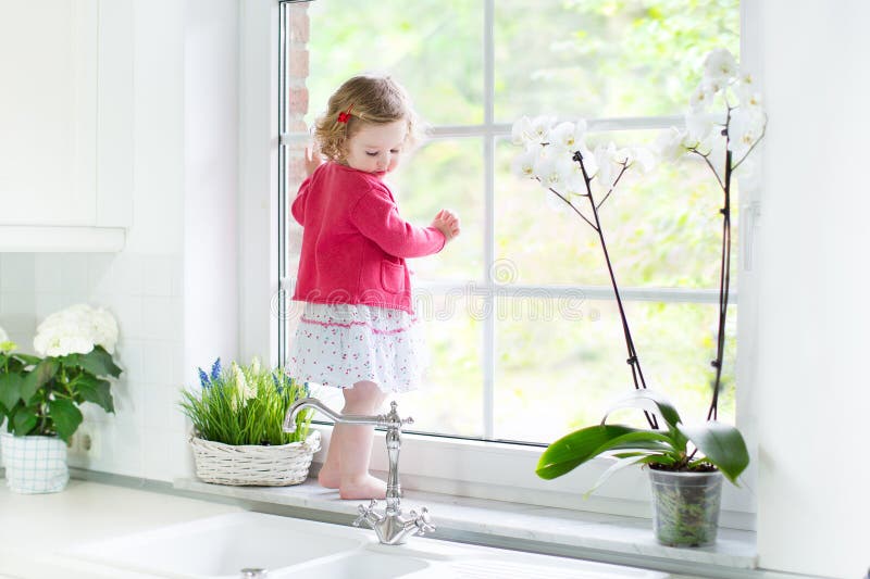 Cute toddler girl watching out window in white kitchen