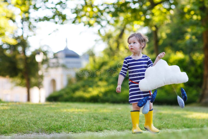 Cute toddler girl in yellow rubber boots and toy with rain drops