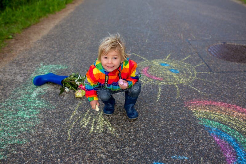 Cute Toddler. Playing in the Rain with Chalks, Drawing on the Asphalt