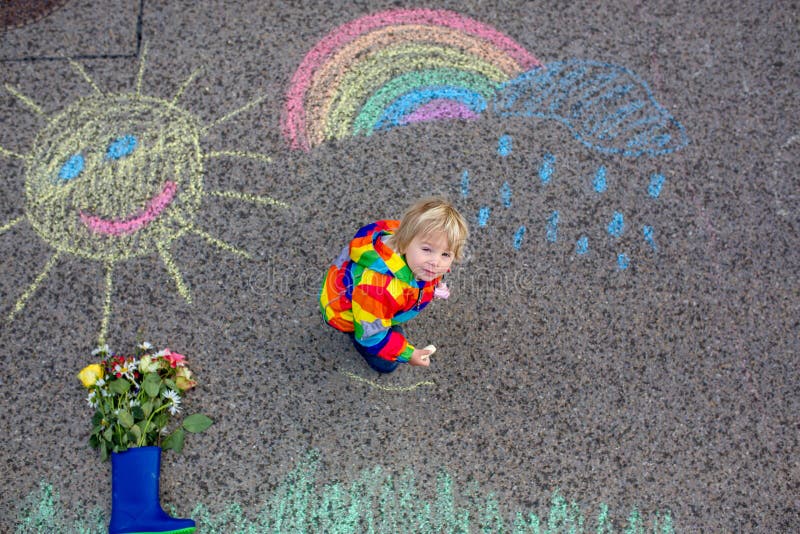 Cute Toddler. Playing in the Rain with Chalks, Drawing on the Asphalt