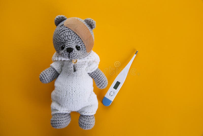 Cute toy bear with sticking plaster and thermometer on orange background, flat lay. Children`s hospital