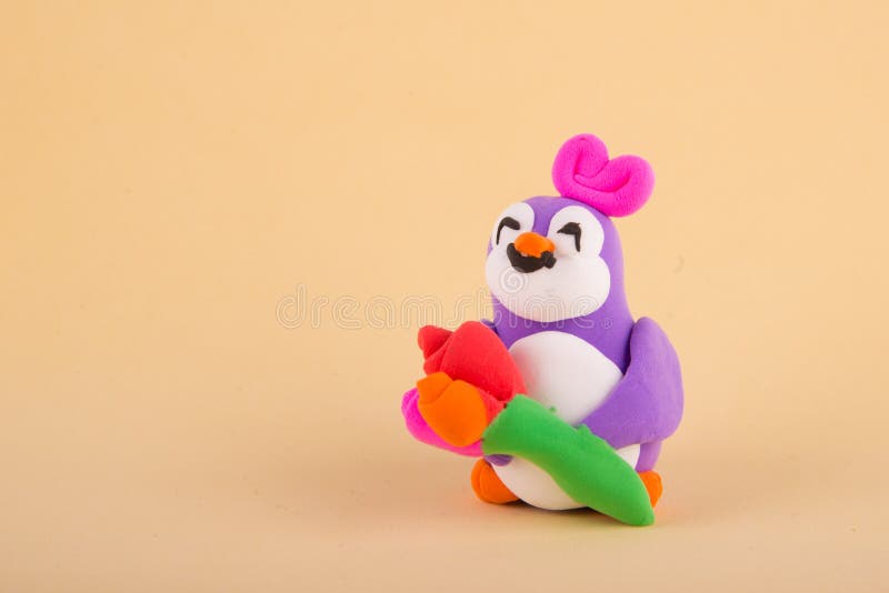 Cute toy girl penguin made of colored polymer, light clay staying on beige background with tulip bouquet