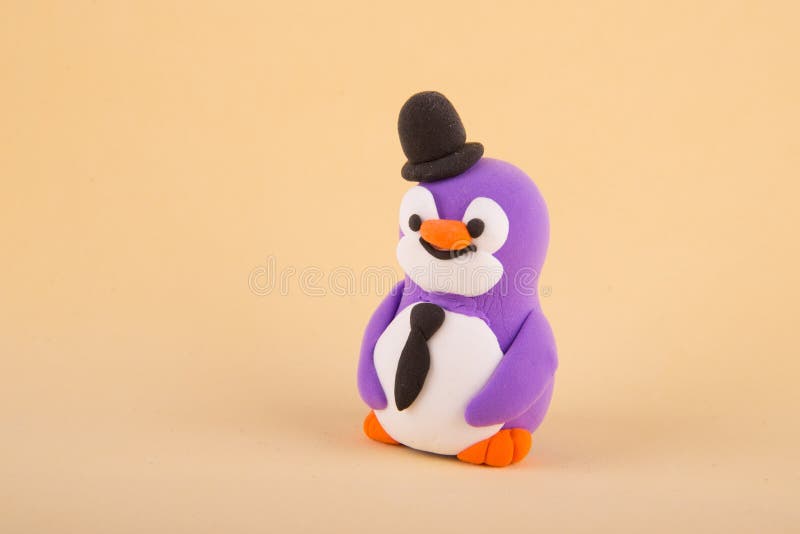 Cute toy penguin with hat and tie made of colored polymer, light clay staying on beige background. Copy space for text. Cute toy penguin with hat and tie made of colored polymer, light clay staying on beige background. Copy space for text