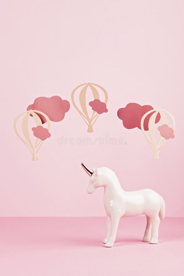 Cute white unicorn over the pink pastel background with clouds and ballons