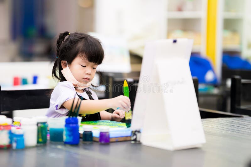 Cute 4 year old Asian girl doing crafts on canvas. Child learn art in class.