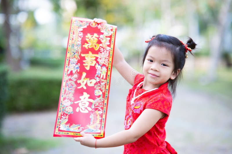 Cute 4 year old Asian kid girl holding red greeting placard with golden Chinese characters meaning Fulfillment.