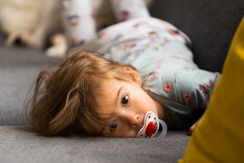 Cute 2 year old Baby girl on a bed on her belly with head on sofa. Bright interior.