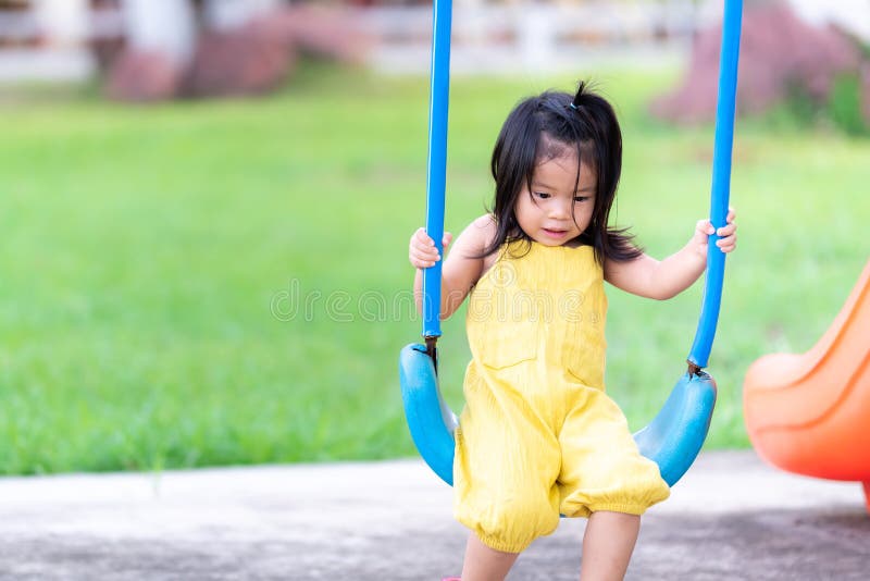 Cute 3-4 year old little girl wearing a yellow dress  the child is playing the blue swing in the playground.