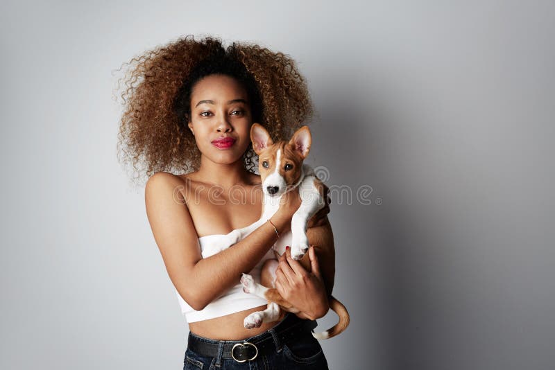 Cute young american african woman with curly hair hugging and kissing her puppy basenji dog. Love between dog and owner