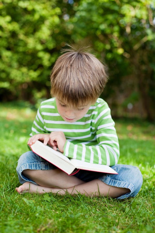 Cute young boy sitting on grass and reading