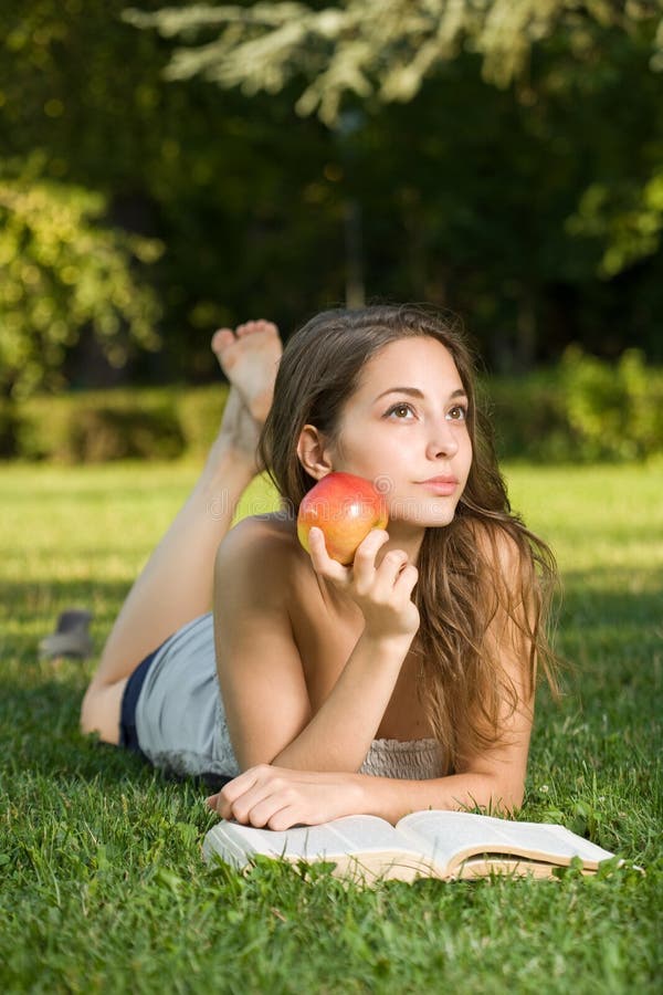 Cute young brunette in the park reading. royalty free stock image