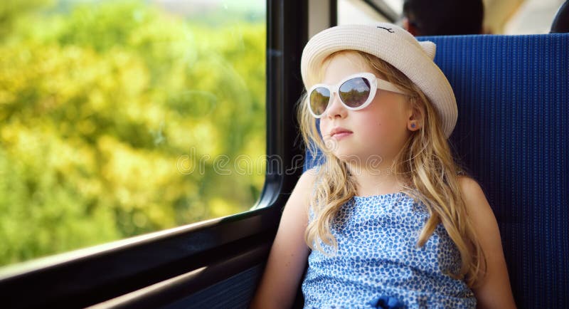 Cute young girl traveling by train on summer day. Child sitting by the window of railway wagon and looking outside