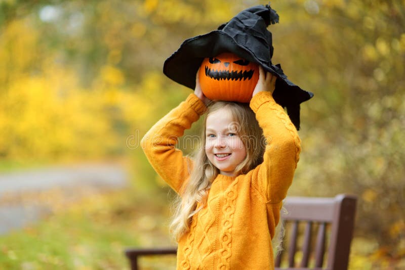 Cute Young Girl Wearing Black Witch Hat Holding a Small Pumpkin. Kid ...