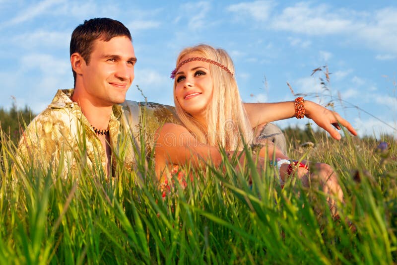 Cute young man and fine woman sit on meadow.