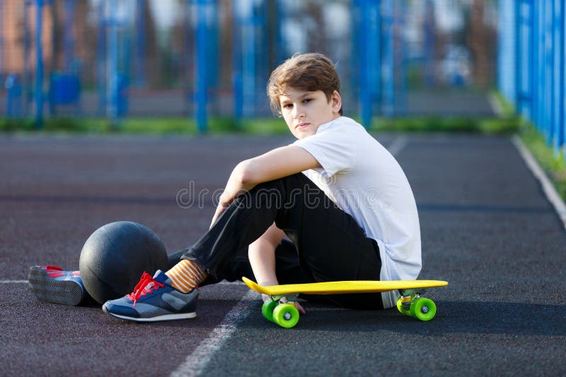 Cute young sport boy with yellow skateboard. He has a good time on his free time on weekend, holidays on sports ground. royalty free stock images Cute young sport boy with yellow skateboard. He has a good time on his free time on weekend, holidays on sports ground. royalty free stock images