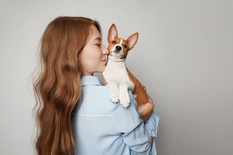 Cute young woman hugging and kissing her puppy basenji dog. Love between dog and owner. Isolated on white background