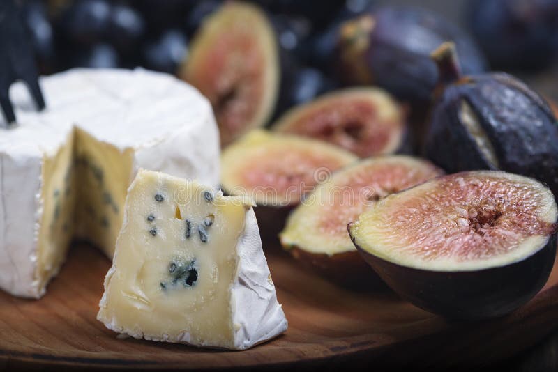 Cuted blue cheese, fresh fig halfs and grapes on rustic wooden plate. Moody scene with selective focus
