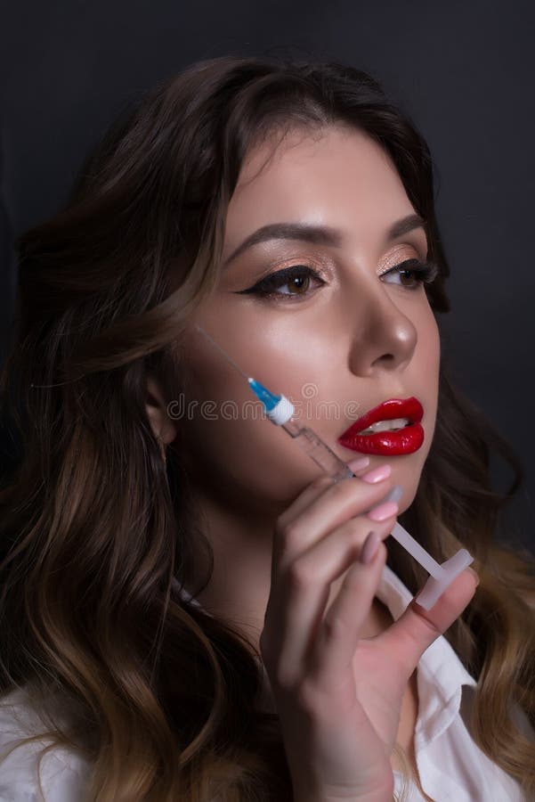 Cuídese en un polo rosado con una jeringuilla Cosmetólogo, cosmetologist en un fondo gris Muchacha hermosa, enfermera medicina fotos de archivo Cuídese en un polo rosado con una jeringuilla Cosmetólogo, cosmetologist en un fondo gris Muchacha hermosa, enfermera medicina fotos de archivo