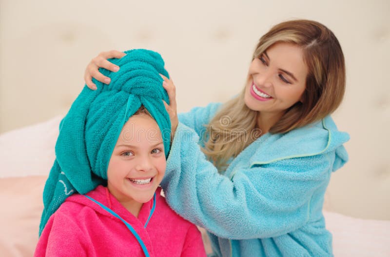 CXlose oben der jungen Mutter, die zu ihrer kleinen Tochter ein blaues Tuch im Kopf aplying ist, während beide das Tragen Bademän lizenzfreies stockfoto