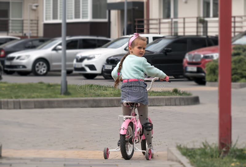 little European girl, with a long pigtail, 5-6 years old, rides a bicycle along the city street, a child's bike ride. little European girl, with a long pigtail, 5-6 years old, rides a bicycle along the city street, a child's bike ride