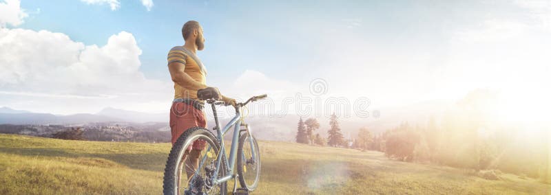 Cycling. Man with bike on a forest road in the mountains on a summer day. Mountain valley during sunrise. Panorama