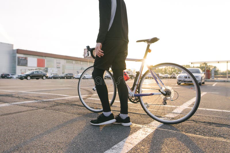 Cyclist in dark sportswear with a highway bike on the background of parking in the sunset stock photos Cyclist in dark sportswear with a highway bike on the background of parking in the sunset stock photos