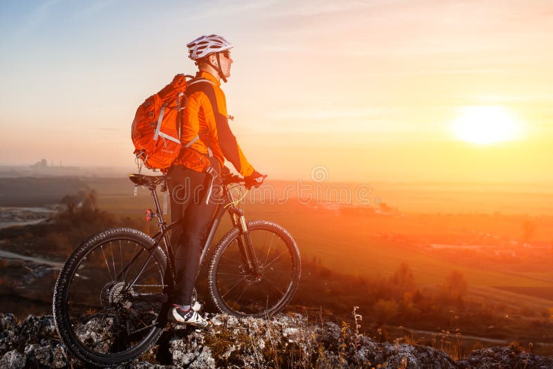 Cyclist leaning against bicycle in front of scenic skyline view of sunset.