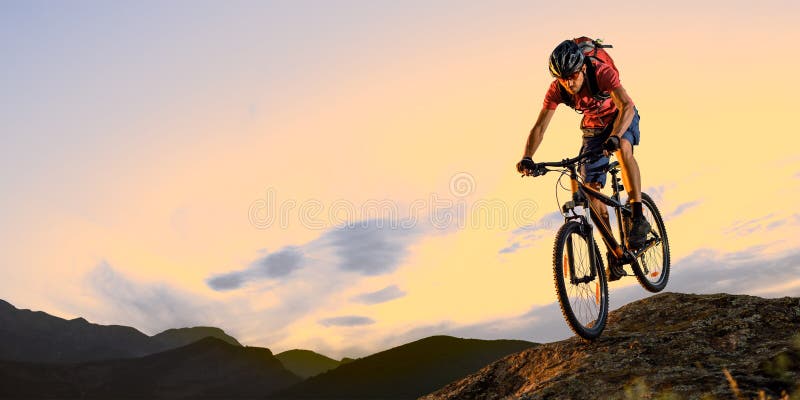 Cyclist in Red Riding the Bike Down the Rock at Sunset. Extreme Sport and Enduro Biking Concept. Cyclist in Red Riding the Bike Down the Rock in the Beautiful