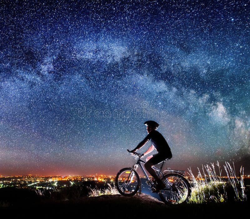 Cyclist riding bike in the night under starry sky