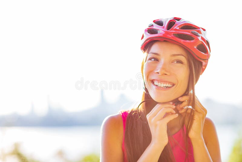 Cyclist woman putting bike helmet on - head protection on outdoor sport activiy or commute lifestyle in city. Asian girl