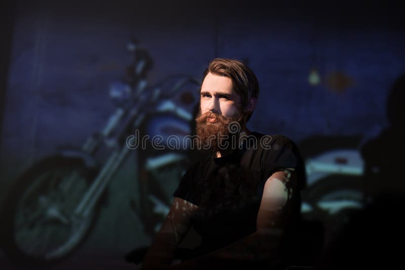 Cycliste barbu brutal d'homme s'asseyant dans une chaise photographie stock libre de droits Cycliste barbu brutal d'homme s'asseyant dans une chaise photographie stock libre de droits