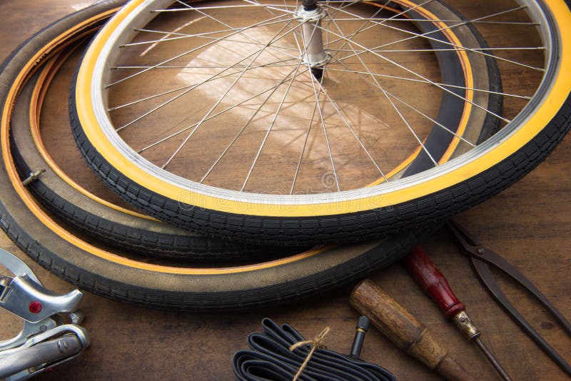 Bicycle repair. Repairing or changing a tire or wheel of an vintage bicycle. Old bicycle wheels on a grungy work desk with well used tools and bicycle parts. Bicycle repair. Repairing or changing a tire or wheel of an vintage bicycle. Old bicycle wheels on a grungy work desk with well used tools and bicycle parts.