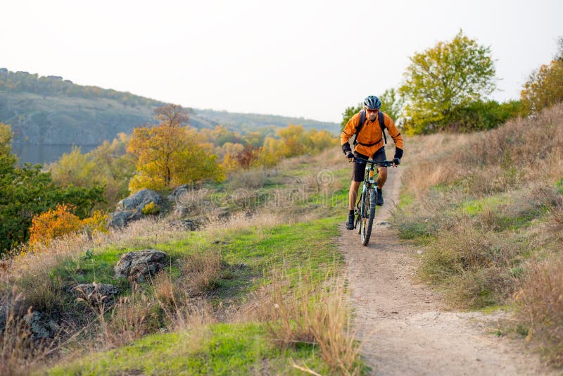 Cyklist i apelsin som rider mountainbiket på Autumn Rocky Trail Extrem sport och Enduro som cyklar begrepp arkivbild Cyklist i apelsin som rider mountainbiket på Autumn Rocky Trail Extrem sport och Enduro som cyklar begrepp arkivbild