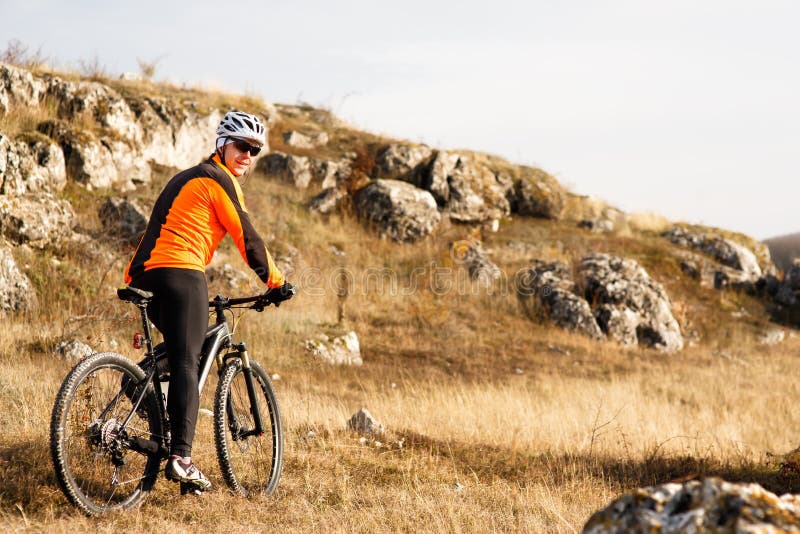 Cyklist i orange omslag som rider cykeln på Rocky Trail Extremt sportbegrepp Utrymme för text royaltyfria bilder Cyklist i orange omslag som rider cykeln på Rocky Trail Extremt sportbegrepp Utrymme för text royaltyfria bilder